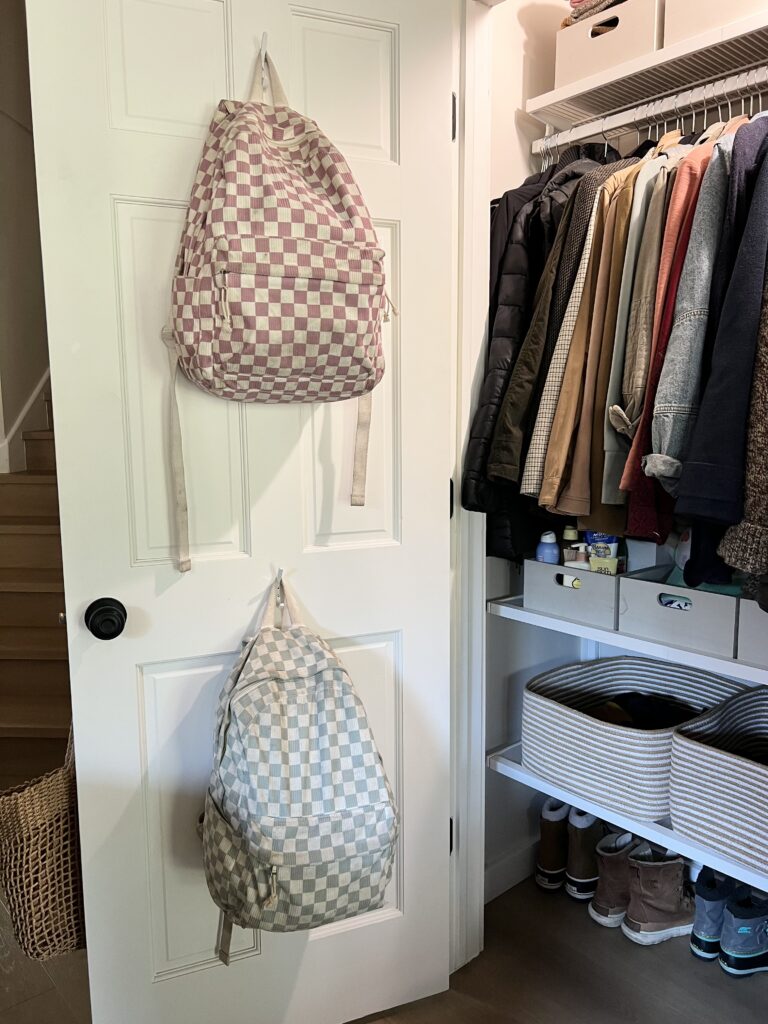 Children’s backpacks hanging on hooks inside an organized entryway closet